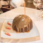 Chocolate dome with warm caramel sauce drizzled over it and fresh strawberries at Maximillien