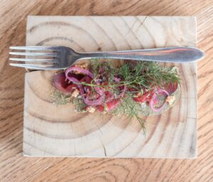 Overhead view of beef tartare with pickled red onion and dill on a wood slice at Overture, Stellenbosch