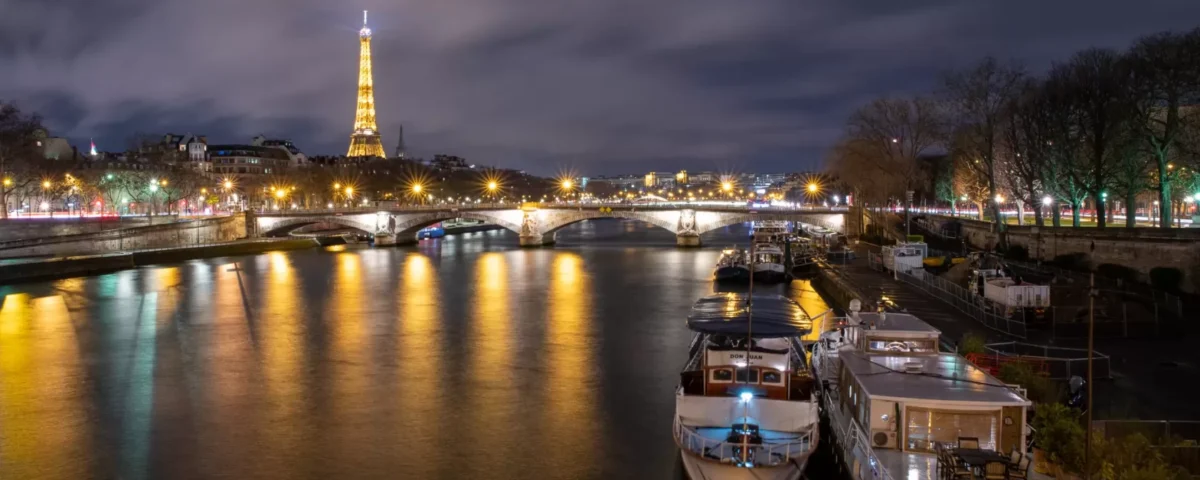 Top 20 things to do in Magical Paris Paris from a bridge with boats and eiffel tower in the background.